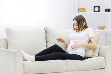 Obraz premium Pregnant woman looking at her stomach on white sofa.