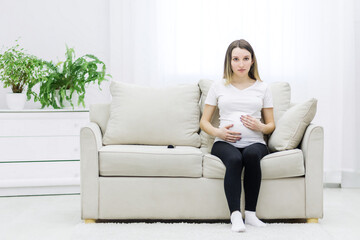Fototapeta premium Pregnant woman sitting on white sofa and touching her stomach.
