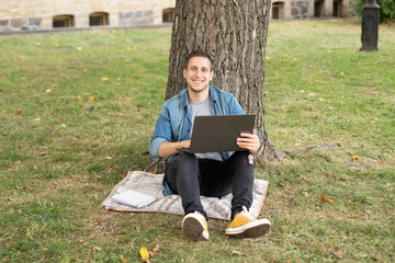 Young man with laptop rest in grass at university campus. Business man sit on lawn work outdoors on...