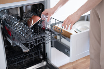 Women's hands sort clean dishes from the dishwasher