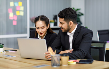 Millennial Asian Indian professional bearded male businessman female businesswoman employee staff in formal business suit sitting working typing laptop notebook computer in company office workplace