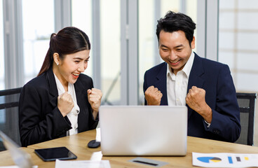 Millennial Asian Indian professional successful bearded male businessman and female businesswoman employee colleague in formal business suit sitting holding fists up celebrating job deal achievement