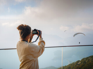 woman enjoys the view from the viewpont over Oludeniz, Turkey. Sunset, clouds, paragliders. Mount Babadag. Female photographer takes pictures of paragliders from observation deck, where their start