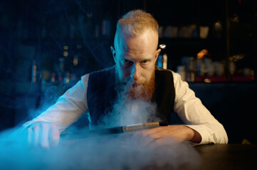 Obraz premium Portrait of stylish bearded man exhales smoke while smoking hookah