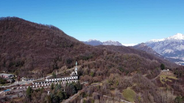  Consonno a 'ghost town' of Olginate, Lecco, in Lombardy, vegetation and snow-capped mountains in the background. Aerial view. 
