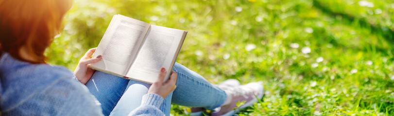 Woman sitting on the blossoming meadow with book in her hands. - obrazy, fototapety, plakaty