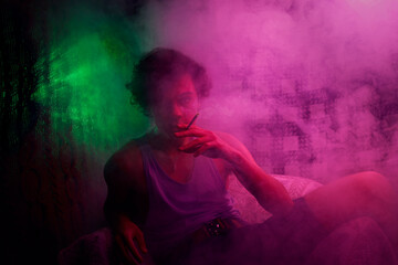 Intoxicated guy smoking cigarette in armchair in colorful smoke