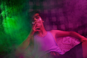 Obraz na płótnie Canvas Defiant teenager with shiny makeyp smoking in colorful smoke