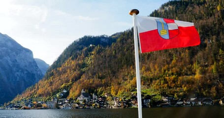 View of Hallstatt, Austria, surrounded by autumn colors, as seen from the ferry, with the ferry's bow flag and regional coat of arms in the foreground