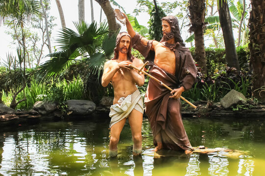 The baptism of Jesus by John the Baptist Statue during the day in a river or pond. Catholic Christian religion statue.
