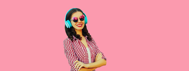 Portrait of happy smiling woman listening to music with headphones wearing sunglasses on pink background