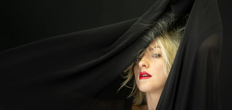 Wide banner portrait of blonde sexy woman fashion model, with red lipstick mouth, behind black cloth, whose hair is electrostatic charged and stick to fabric cloth