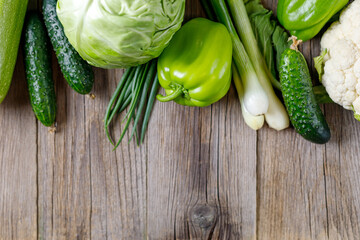 Border of green raw vegetables on wooden background. Top view of healthy organic food. Copy space