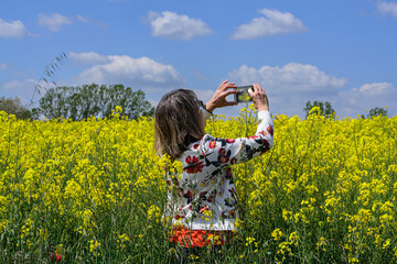 woman taking a photograph with her smartphone of a field of yellow flowers.