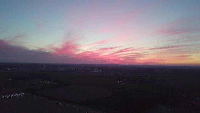 Incredible pink sunset over rural English agricultural fields with standing water and puddles. Countryside community. Drone shot tracking backwards and jibbing down to show more segregated fields.