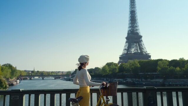 Attractive woman with yellow bicycle looking at the Eiffel Tower from the bridge