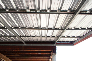 Roof silver steel strong metal structure large made with plate aluminum. Bolts attached to each other, durable from strong winds. Strong garage sunlight shines. Attached to side of wooden house.
