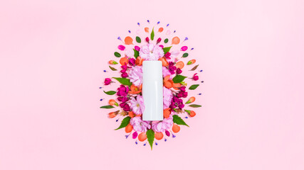 Natural flower heads, buds and leaves around a white cosmetic tube. Pink background with copy space. Flat lay
