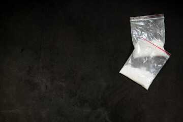 Cocaine powder lines, rolled banknote and drugs in plastic bag pocket on black glass surface background, top view. Drug addiction concept