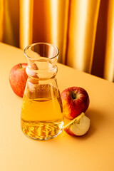 Glass decanter with apple juice and ripe apples on kitchen table and yellow background. Healthy drink concept with copy space