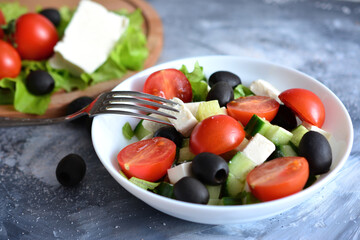 A white bowl with greek salad with cherry tomato, feta cheese and a fork