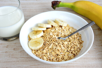 A bowl of oatmeal with banana slices and glass of milk, close-up