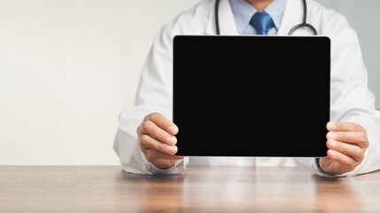 Doctor holding a black blank screen tablet while sitting at the table in the hospital