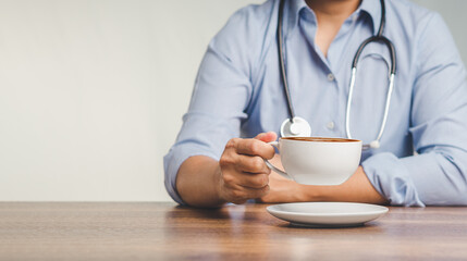 Doctor with a stethoscope holding a coffee cup while sitting at the desk