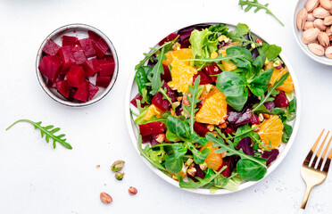 Beet and orange healthy salad with arugula, lamb lettuce, mini chard and pistachios, white kitchen table, copy space. Fresh useful vegan dish for healthy eating