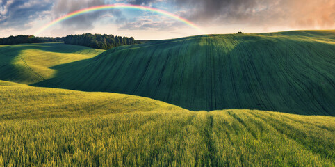 Rainbow and dramatic gray sky with clouds landscape. picturesque hilly field
