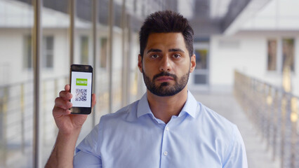 Medium shot of indian young man showing qr-code and covid19 passport on cellphone