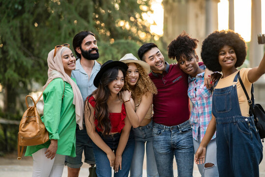 Multiethnic guys and girls taking selfie outdoors with backlight - Happy lifestyle friendship concept about young multicultural people having fun together in the city