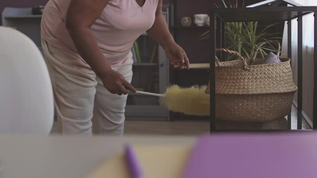 Cropped shot of unrecognizable Black woman using feather duster while cleaning living room