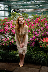 portrait of beautiful romantic redhead woman in pink dress with flowers in spring garden