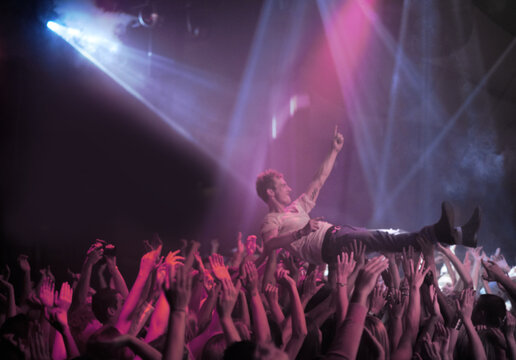 Surfing on a wave of praise. A stage diver being carried across the audience at a rock concert. - Powered by Adobe