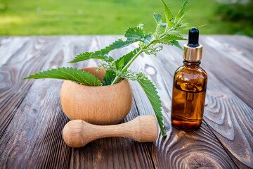 Leaves of young fresh nettle in a wooden mortar. Preparation of elixirs and efir oils from summer herbs. Cosmetic bottle with a pipette on a wooden table.