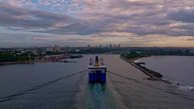 Back view of ferry boat entering in port with Santo Domingo city in background on cloudy day, Dominican Republic. Aerial drone view