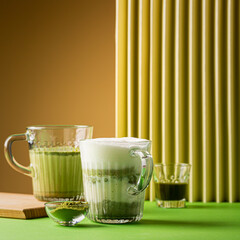 Matcha green tea latte in a glass on green yellow background. Healthy vegan drink with plant based...