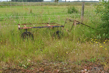 Old Rusty Wheeled Trolley Overgrown in  Field beside Wire Fence 