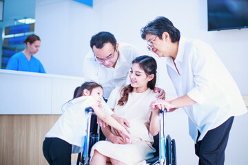 Asian young husband touching wife’s pregnant belly relaxing sitting on wheelchair in hospital....