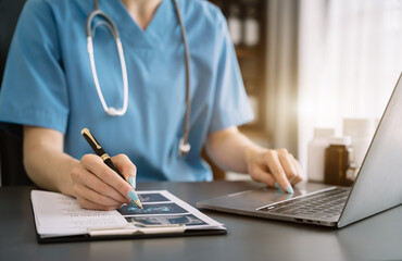 Doctor working on laptop computer, writing prescription clipboard with record information paper folders on desk in clinic, Healthcare and medical concept.