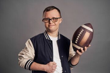 Man with down syndrome holding ball for american football on gray background