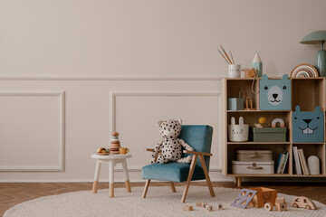 Minimalist composition of kid room interior with copy space, blue armchair, wooden sideboard, beige rug, plush toys, wooden blockers, wall with stucco and personal accessories. Home decor. Template.