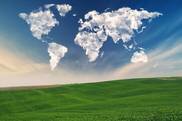 Fototapeta na wymiar clouds in the form of a world map over a green field. Travel and landscape concept. hilly field