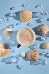 Cup of coffee with sea shells, ice, water drops on the blue background. Coffee latte with seashells in the middle of the table. Coffee break on  island. Happy day, morning. Enjoying vacation.