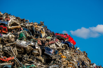 Front view of a red car atop a pile of compressed and crumpled car wrecks in a junkyard, conveying...
