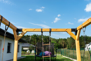 A modern cubic playground made of wooden logs and metal corners, visible nylon ropes and clip hook.