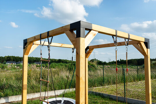 A modern cubic playground made of wooden logs and metal corners, visible nylon ropes and clip hook.