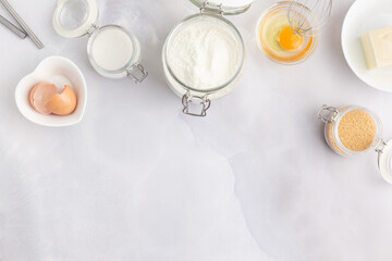 Obraz na płótnie Canvas Various baking ingredients - flour, eggs, sugar, butter and kitchen utensils on grey background. Top view.