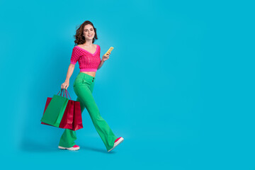 Full length photo of lovely stylish lady wear trendy clothes carry packages walking street go empty space isolated on blue color background